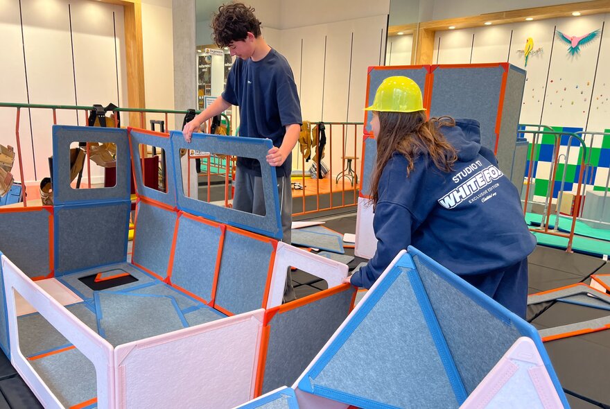 Two kids building cubby houses out of large cardboard panels.