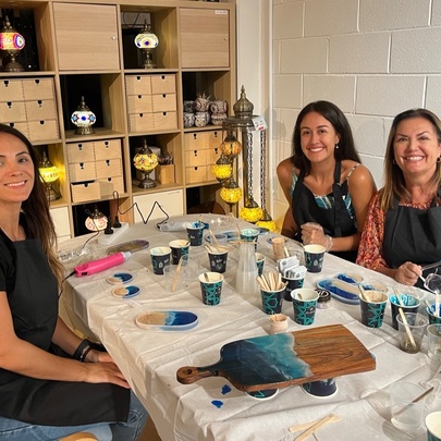 People seated around a crafts table in a studio, with pots of resin and other tools and equipment on the table.