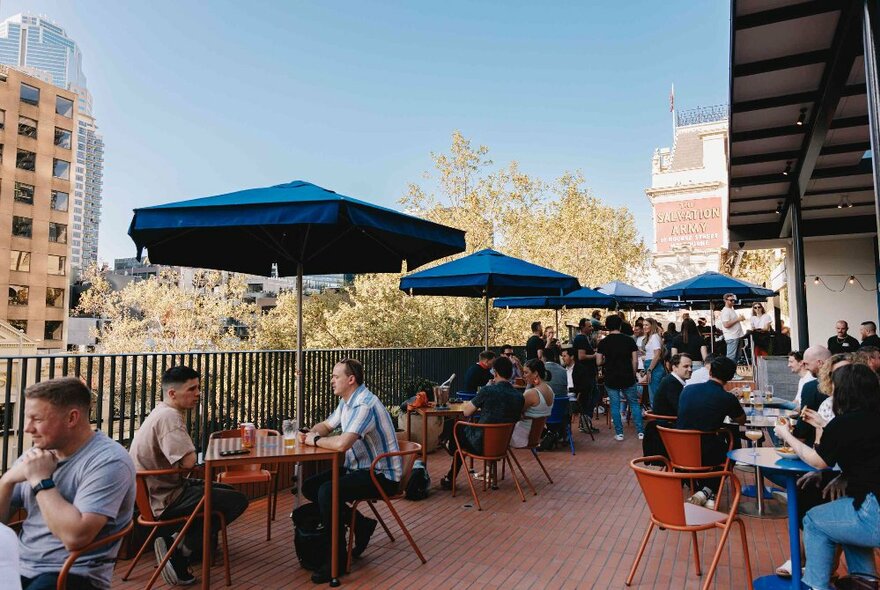 People seated outside under shade umbrellas at a rooftop bar