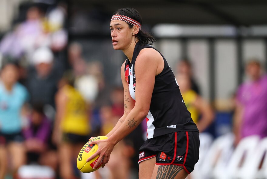 An AFLW player in a St Kilda jersey about to kick a yellow football during a game.