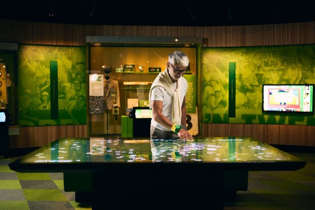 A person looking at an interactive digital tabletop in a room with green murals on the walls.