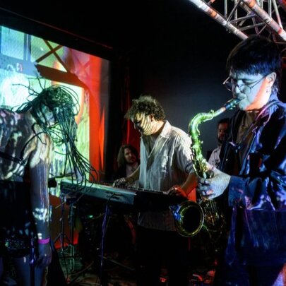 Three musicians performing on a small stage with coloured lights. 