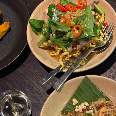 Dishes of Asian food with cutlery and glass on a table.
