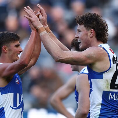 Two North Melbourne AFL football players clapping hands during a match.