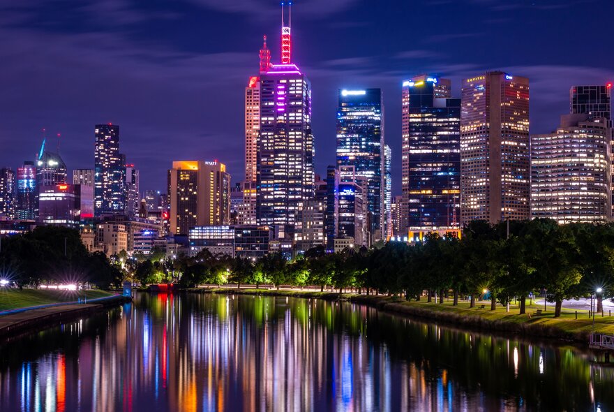 Melbourne city skyline at night with illuminated buildings reflected in the Yarra River.