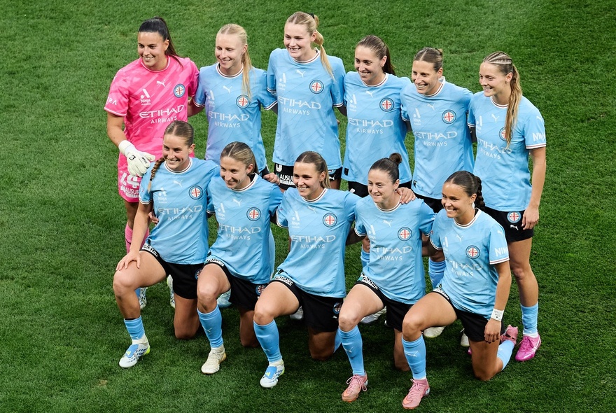 Women's soccer team posing in two ranks, one line standing while the line in front kneels, on an oval.
