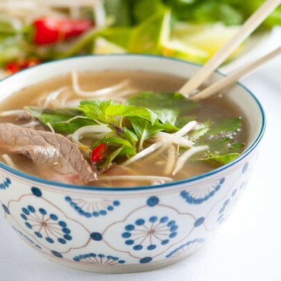 A bowl of beef pho with chopsticks sticking out the top. 