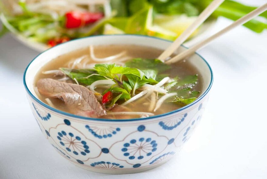 A bowl of beef pho with chopsticks sticking out the top. 