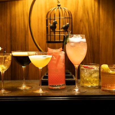 Drinks lined up on a shelf and wooden wall in front of a birdcage ornament.