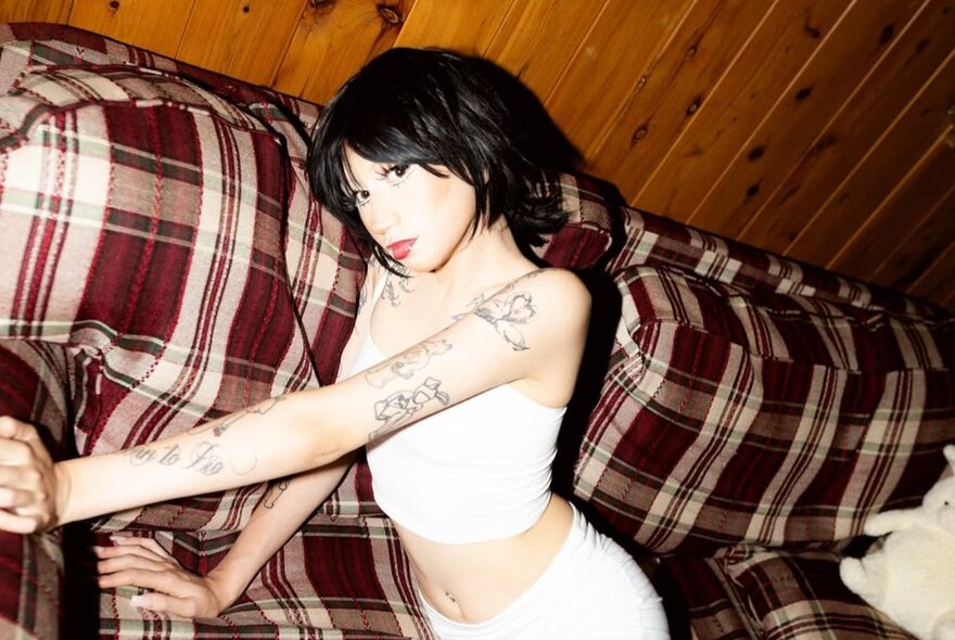 Singer Cherry Rype posing on a checked sofa in a wood-lined room