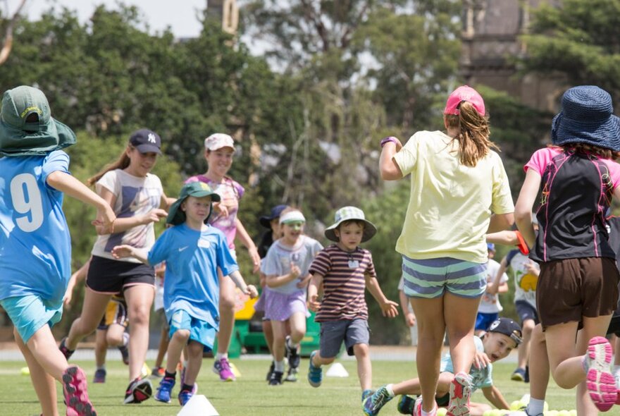 Group of primary school-aged children running around outdoors on a green lawn.