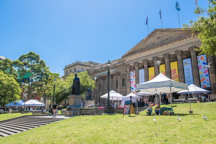 State Library Victoria lawn with umbrellas and seating on the grass.
