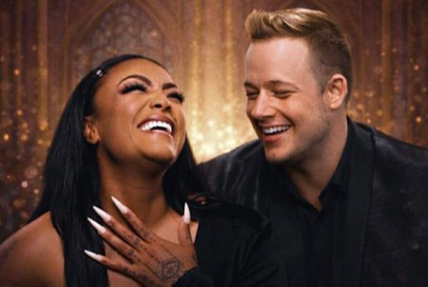 Vocalists Emily Williams and Greg Gould smiling in front of a gold sparkling backdrop.