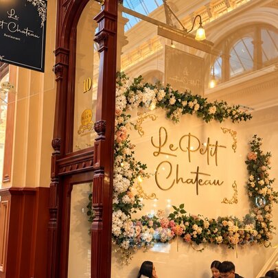 A decorated storefront inside a vintage arcade, featuring a large white floral display wall with the words 'Le Petit Chateau' written in elegant script.