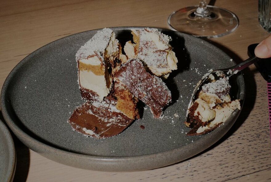 A spoon being used to break into a cake like dessert on a ceramic plate.