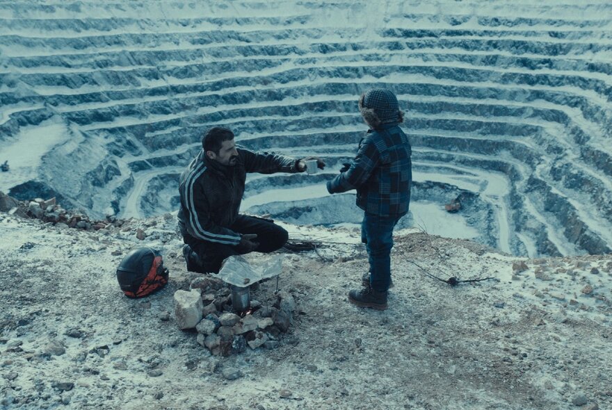 A still image from a film showing two people on the edge of a terraced, rocky landscape.