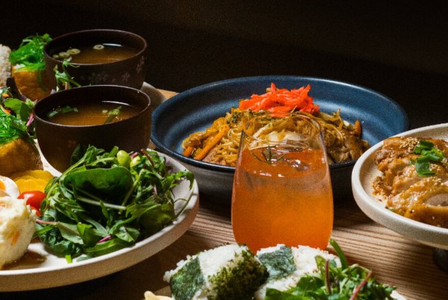 A selection of Japanese food items on plates, and drinks, on a wooden table.