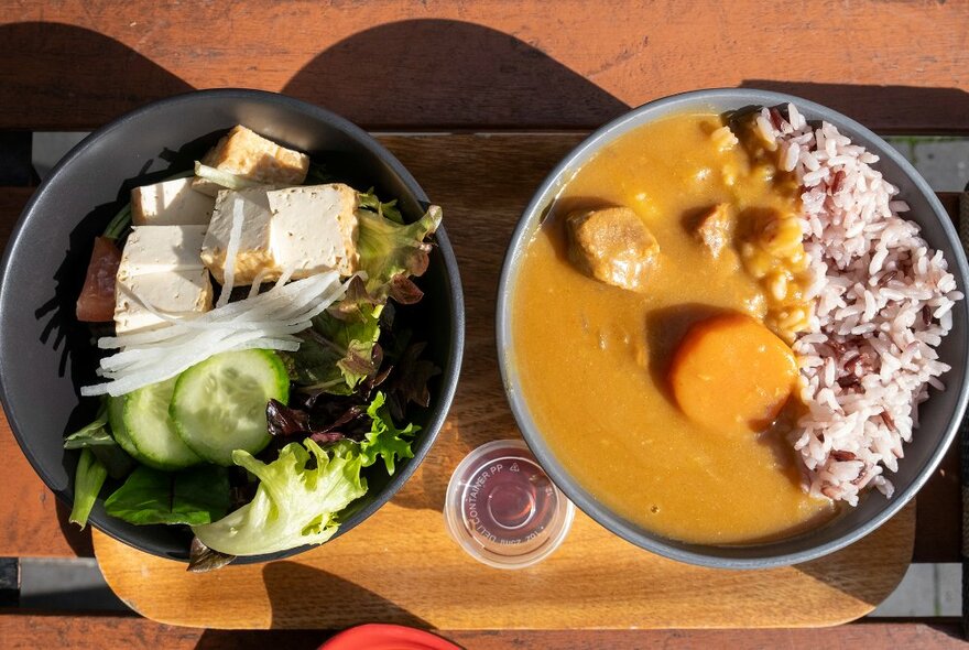 A tray with a bowl of curry with rice and a bowl of salad.