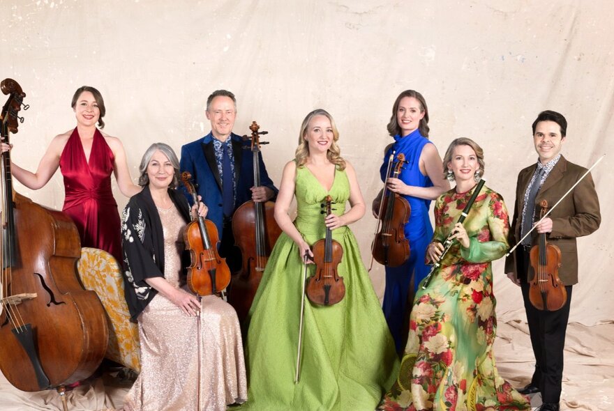 A row of classical musicians wearing formal gowns and suits, holding stringed instruments.