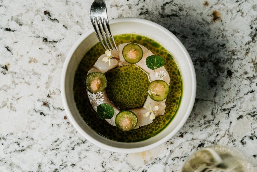 A bowl of food on a restaurant's dining room table with a fork resting on it.