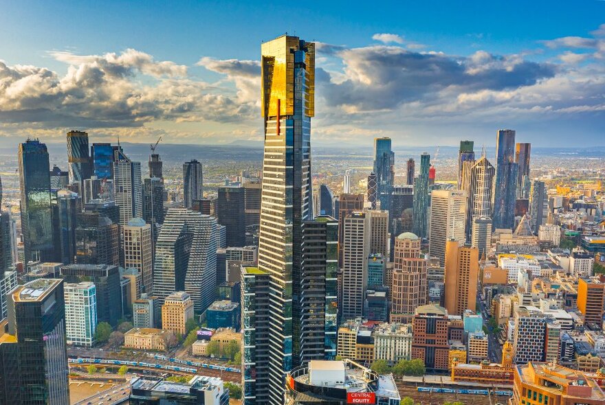 Gold-plated Eureka Tower skyscraper and cityscape against the city skyline and blue sky with clouds.