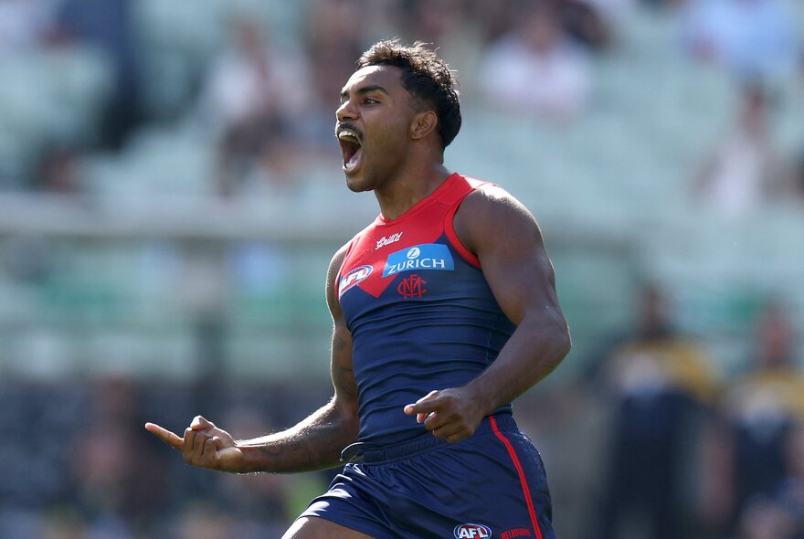 A Melbourne AFL player running and cheering himself and the crowd on during a match.