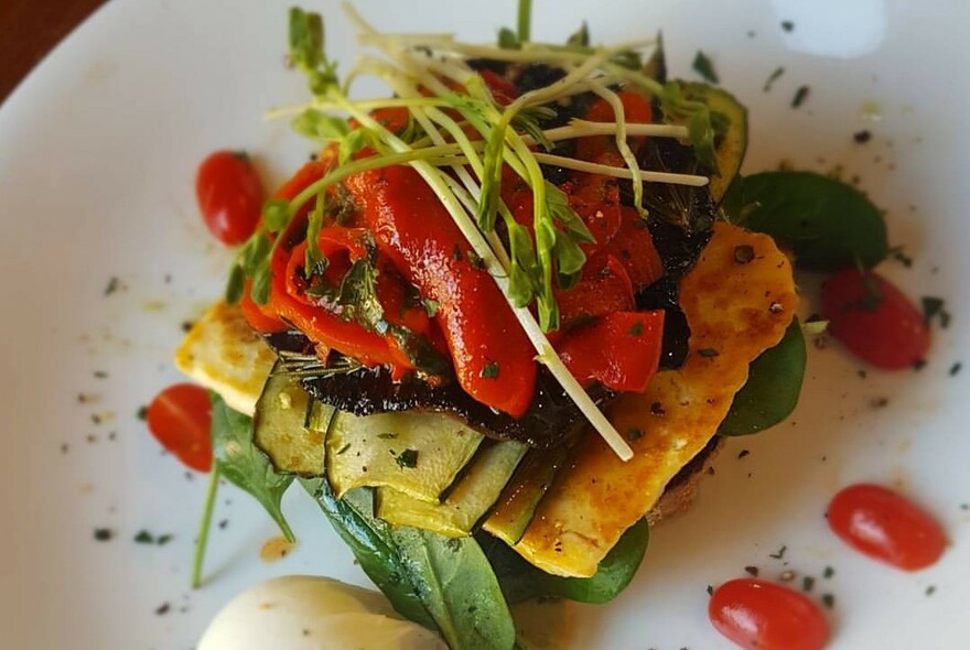 A vegetable stack on a plate accompanied by tomatoes and dressing.