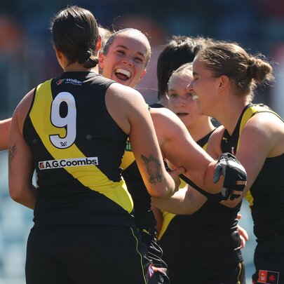 Richmond AFLW players celebrating on the field, coming together for a group huddle.