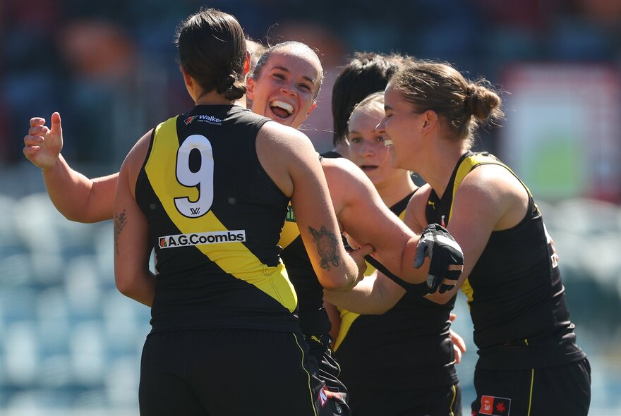 Richmond AFLW players celebrating on the field, coming together for a group huddle.