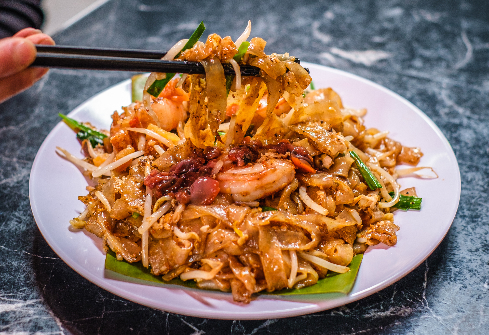 Char kway teow noodles on a plate, being lifted with chopsticks.