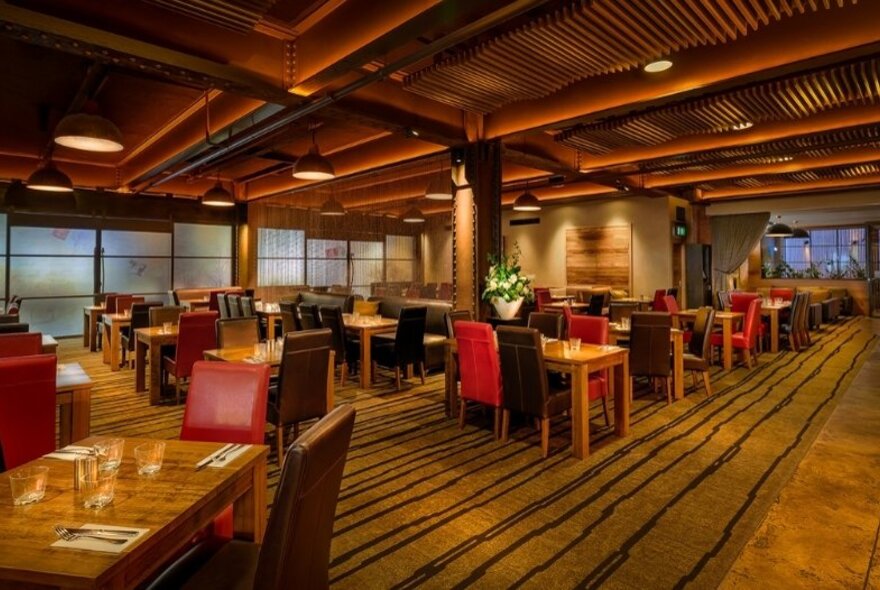 An empty restaurant area with many tables and red chairs. 
