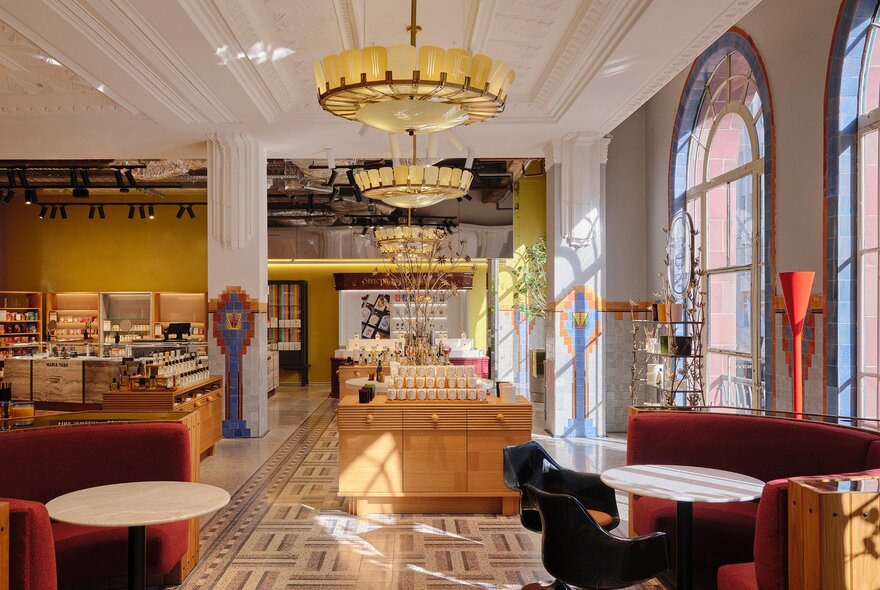 Inside an art deco-style store with large arched windows, a chandelier and displays with perfume on them.