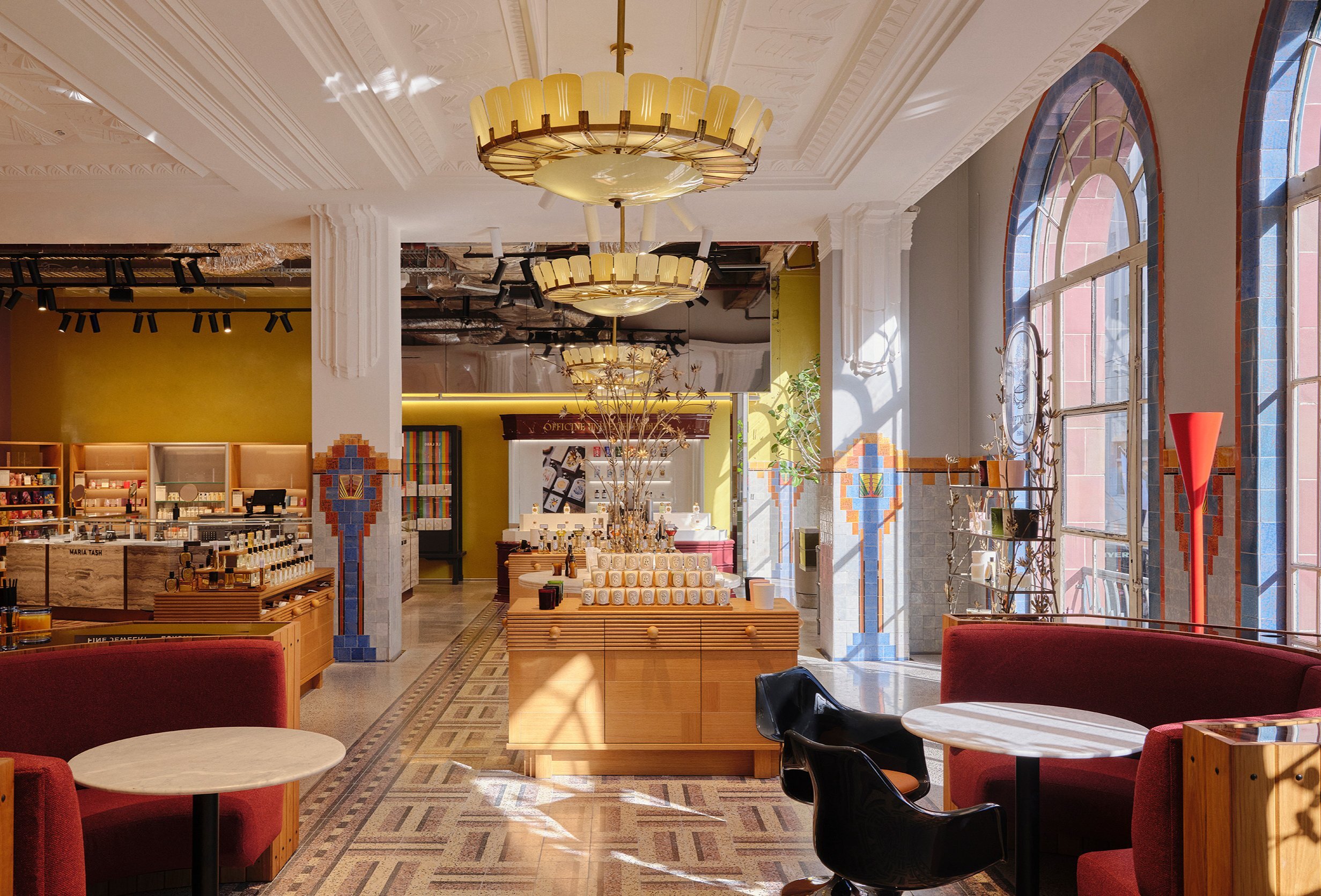 Inside an art deco-style store with large arched windows, a chandelier and displays with perfume on them. 