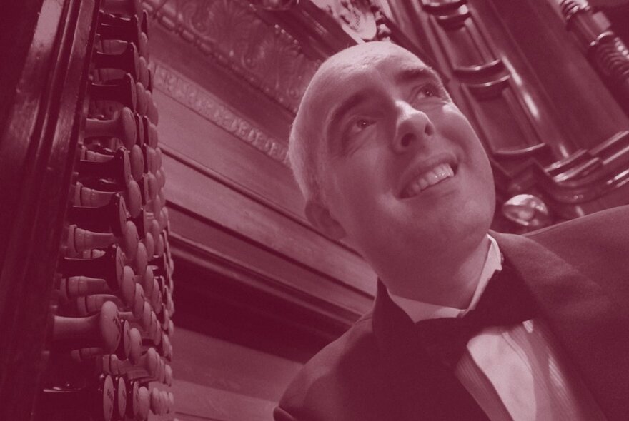 Smiling face of organist Thomas Heywood posed in front of the Melbourne Town Hall's Grand Organ; sepia toned image.