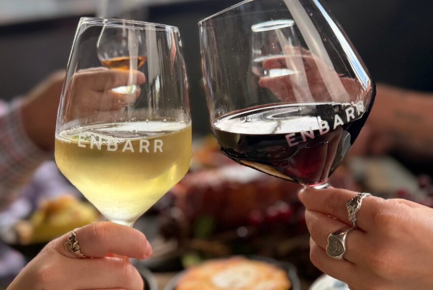 Two hands holding a glass of white wine and a glass of red wine.