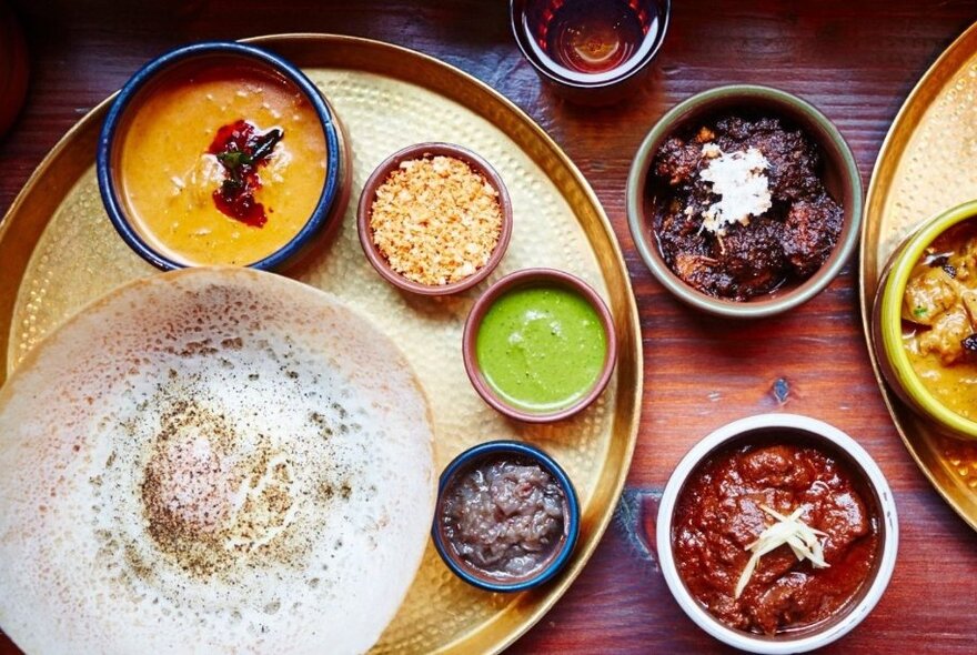 Looking down at lots of small plates of Sri Lankan food and condiments. 