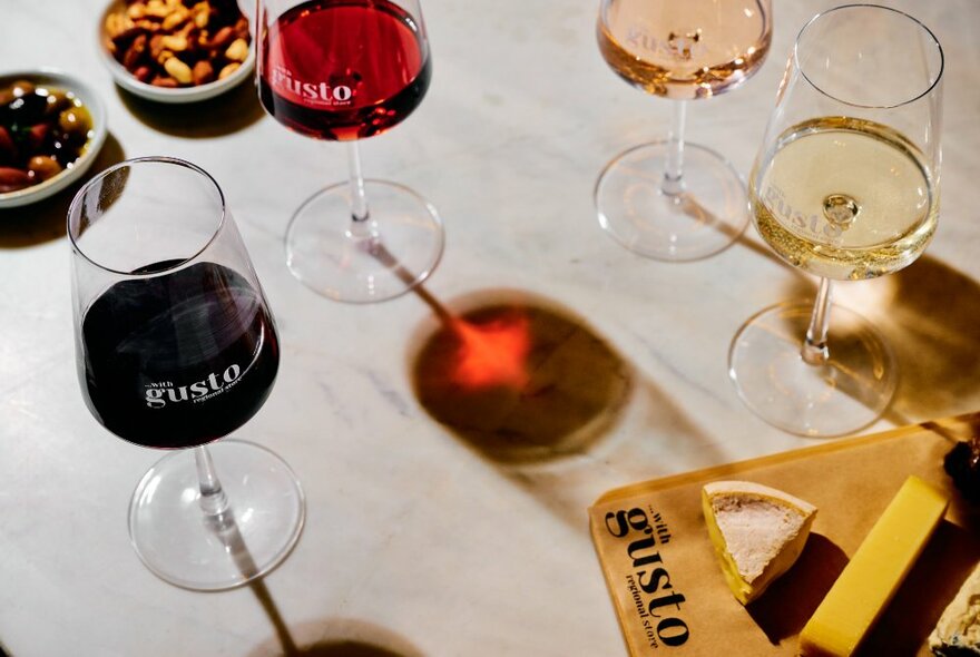 Four glasses of wine, red, light red, rose and white, next to bowls of snacks and a cheese board.