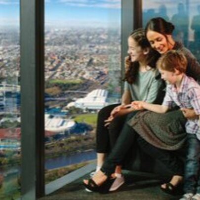 A mother and her two children sitting in front of a glass window looking out over the city of Melbourne.