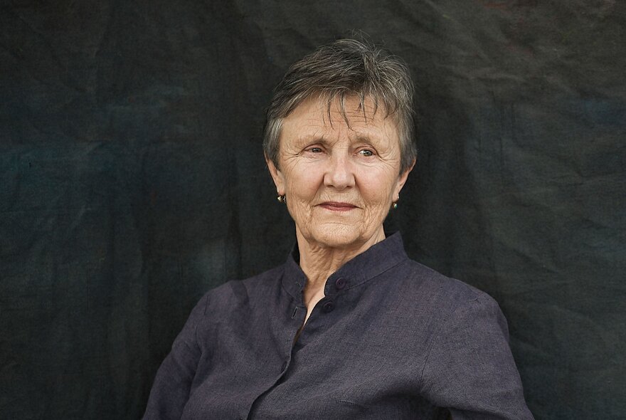 Writer Helen Garner, an older woman with short hair, looking off camera, wearing a collarless dark purple shirt.