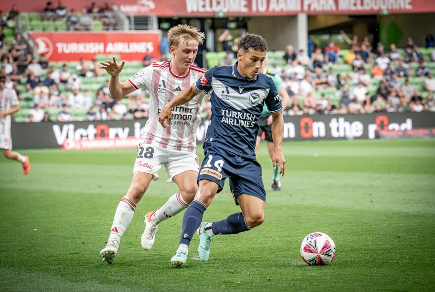 A soccer match with two players going after a soccer ball in front of a crowd. 