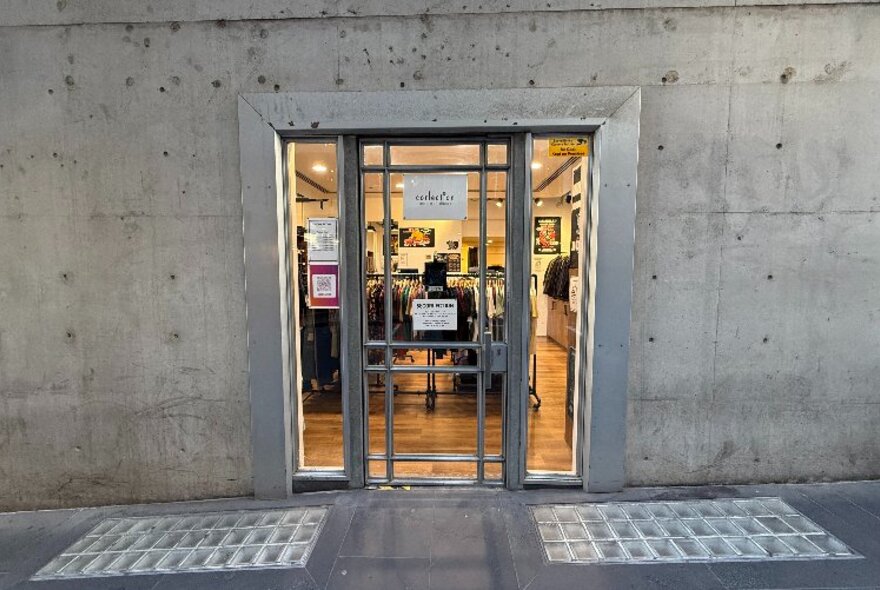 Exterior of a store with a glass door set in the middle of a concrete wall.