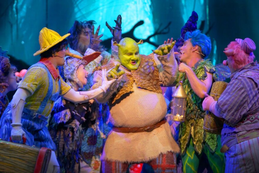 The cast of Shrek The Musical on a theatre stage performing and singing.