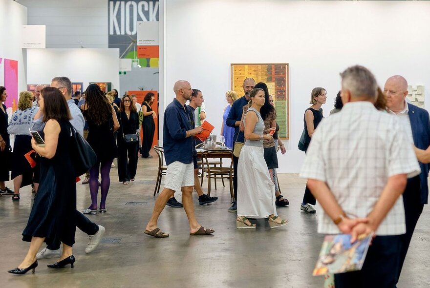 People walking through a large gallery space hung with large artworks.