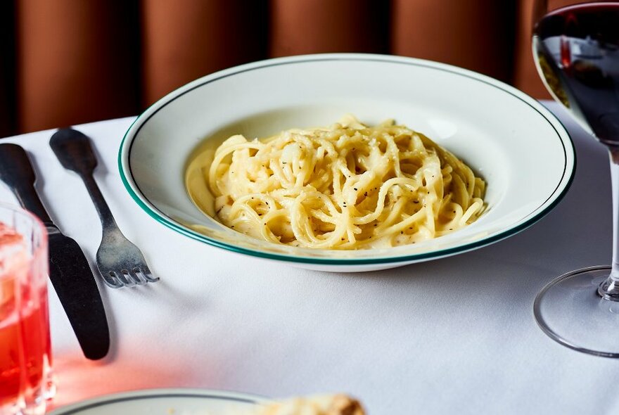 Table setting with a bowl of spaghetti, cutlery and a glass of wine.