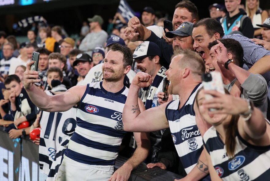 Geelong players posing with fans for selfies and looking happy. 