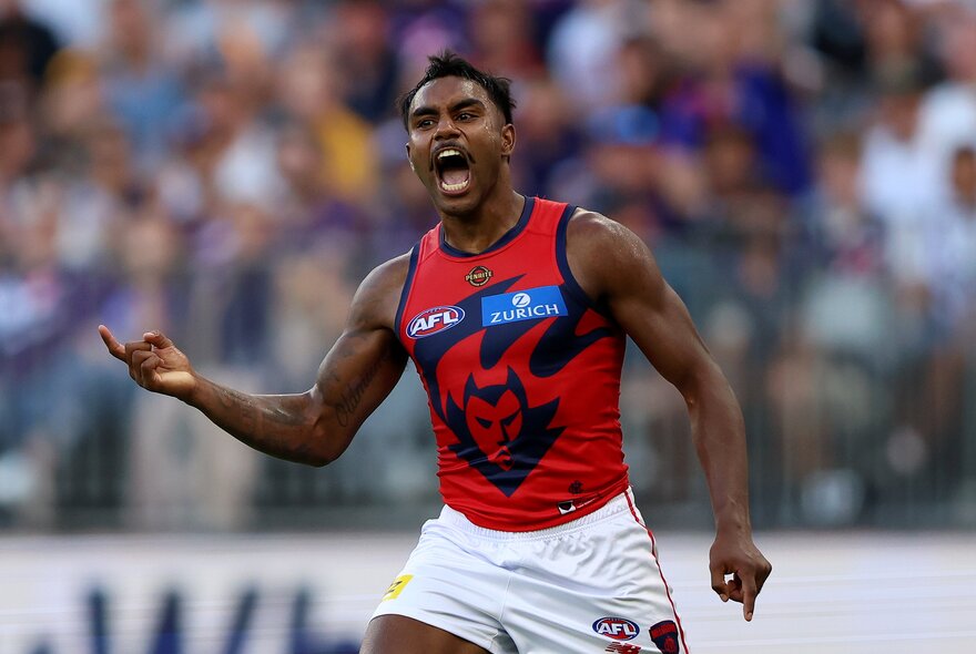 A Melbourne AFL football player on the field during a match with his arms in the air cheering himself on.