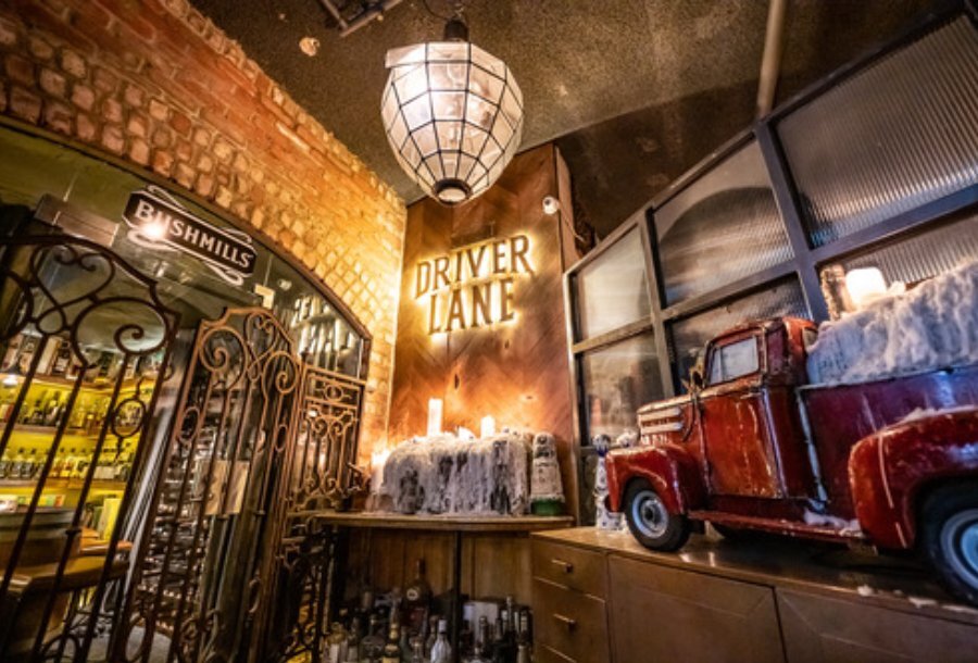 A neon sign inside an old vintage building next to a red toy truck with old candle wax, an old gate and alcohol bottles.