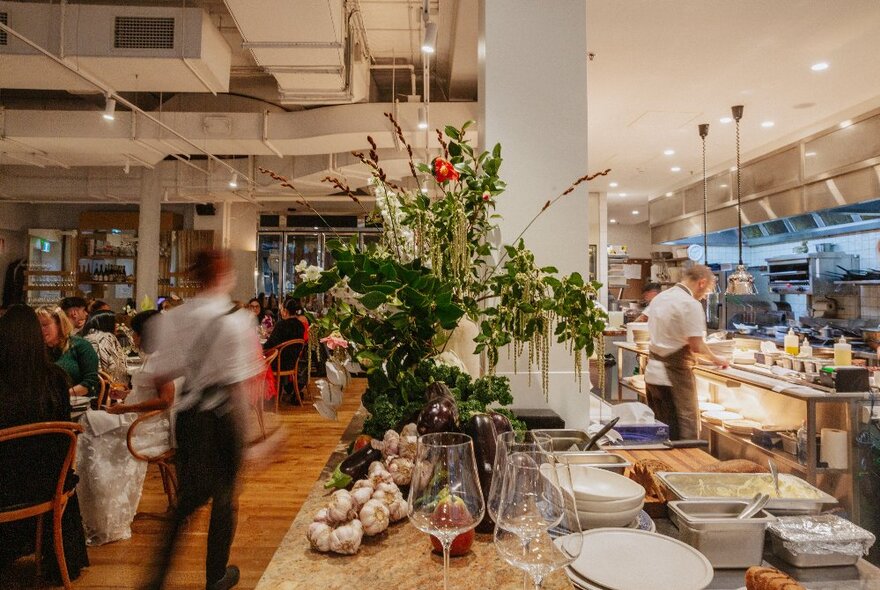 The interior of Hazel restaurant with views of the busy kitchen, the food plating up section and the restaurant dining room with patrons seated at tables.