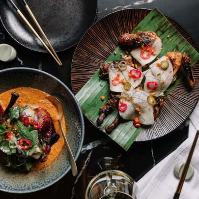Looking down on two Asian style dishes, one on pandan leaves and another in a red curry sauce. 