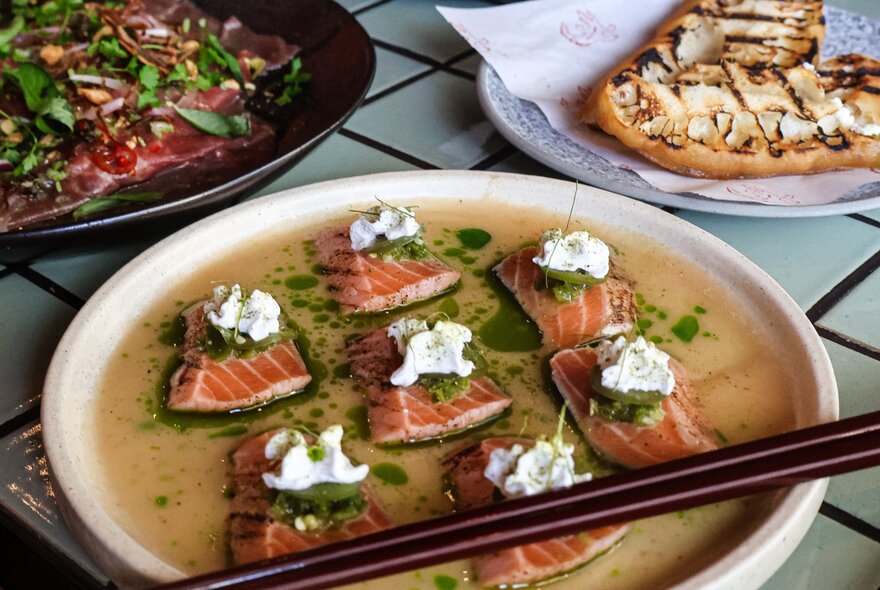Plate of tuna crudo with chopsticks, topped with white sauce.